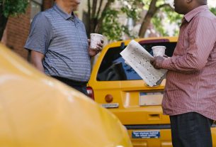 Crop anonymous multiracial taxi drivers with takeaway coffee and newspaper speaking near yellow cars in town — Gambiva Casino