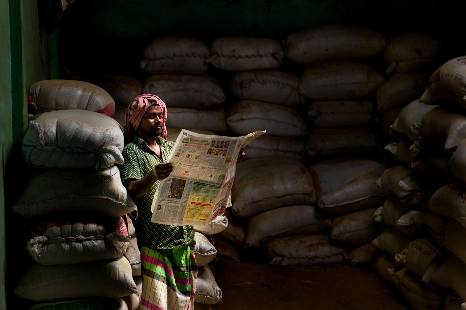 A man in traditional attire reads a newspaper in a dimly lit storeroom with stacked sacks. — Was unterscheidet Dracula Casino